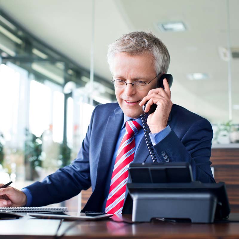 Man on a phone call A man in a suit and tie talking on a desk phone.