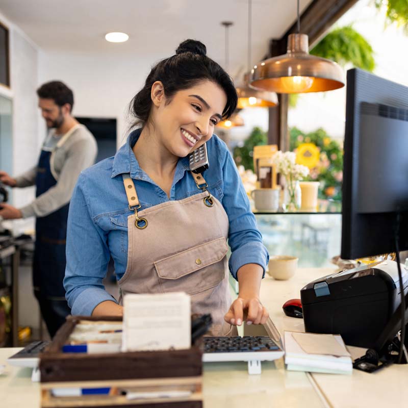 Smiling woman working at cafe Woman with apron smiling in front of computer while talking on the phone
