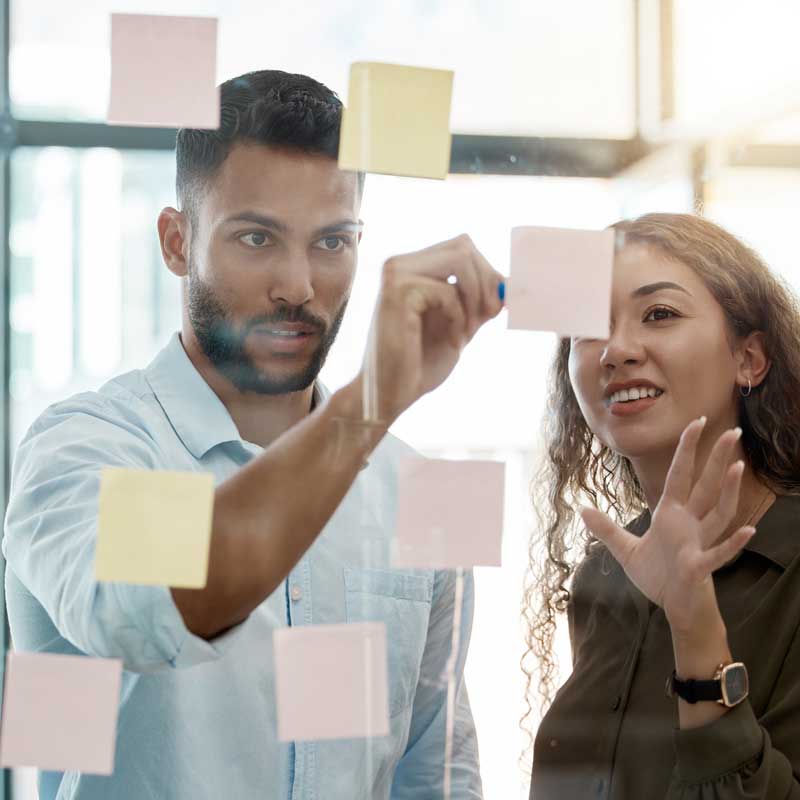 Two people brainstorming ideas on whiteboard with sticky notes