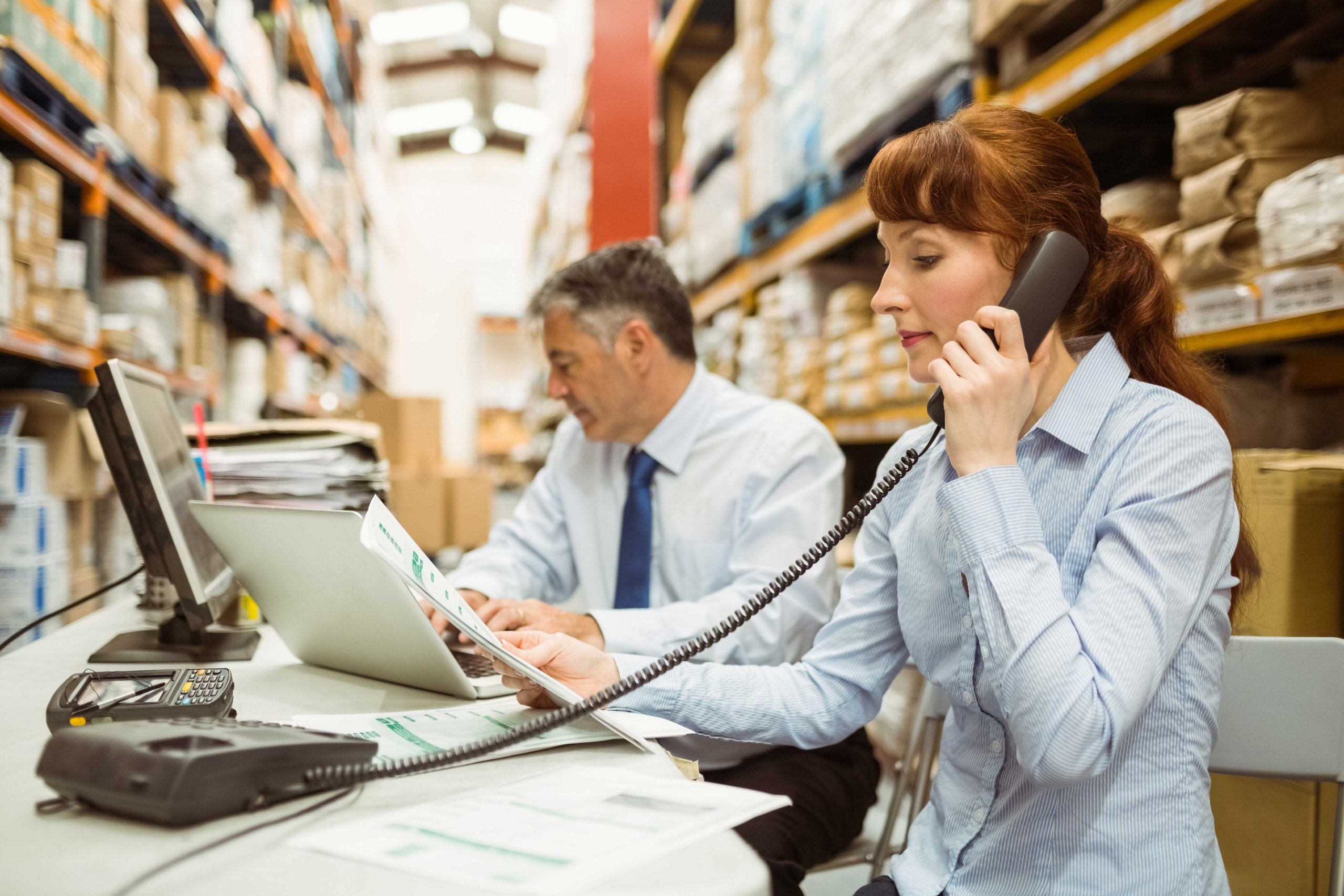 Warehouse worker using modern phone system while looking at notes